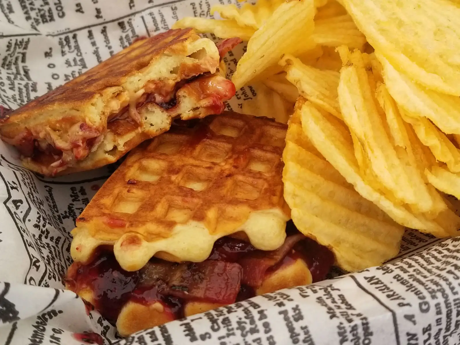 A waffle sandwich with cheese and bacon, and a side of kettle chips A waffle sandwich with cheese and bacon, and a side of kettle chips