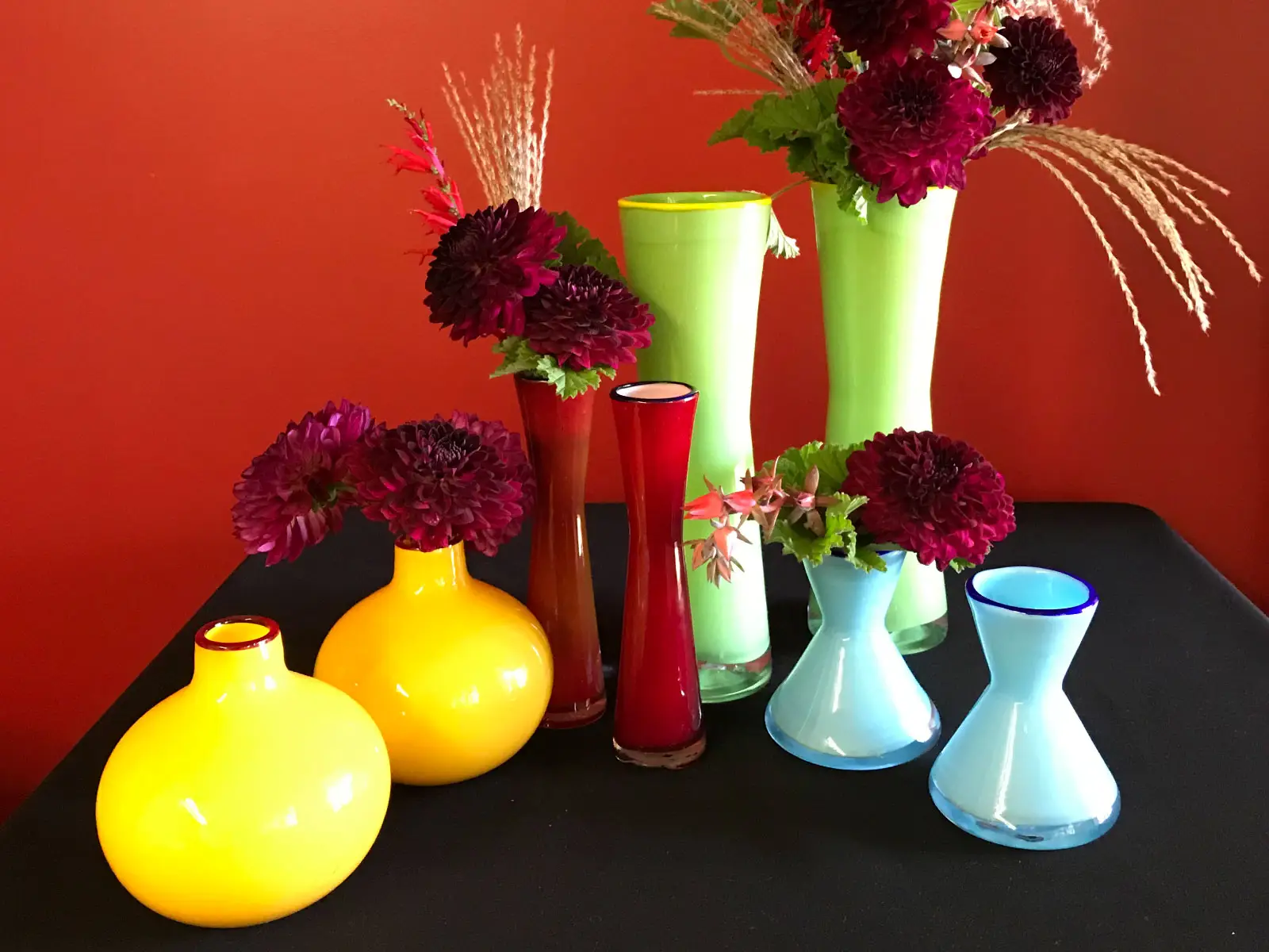 Sets of orange, red, green and blue vases with purple flowers in each one Sets of orange, red, green and blue vases with purple flowers in each one
