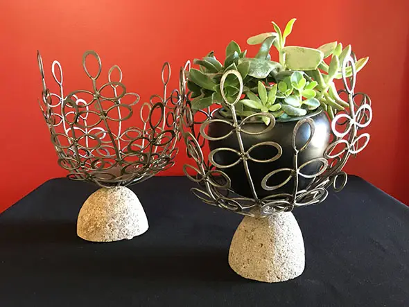 A flower pot of small green-leaf plants set in a designed metal cradle on top of decorative stone A flower pot of small green-leaf plants set in a designed metal cradle on top of decorative stone