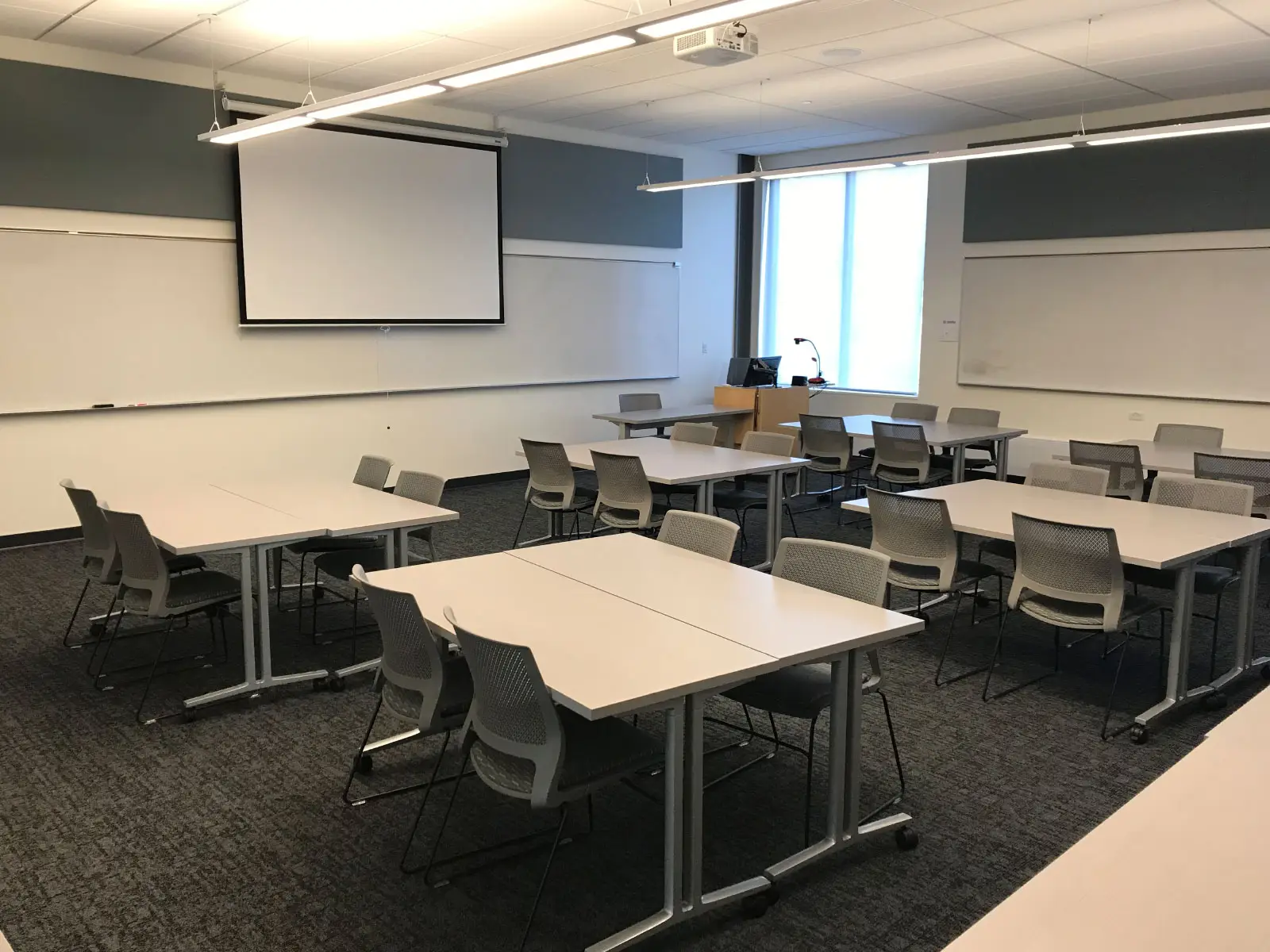 Several tables with chairs in front of a projector screen in a Oregon City campus classroom Several tables with chairs in front of a projector screen in a Oregon City campus classroom