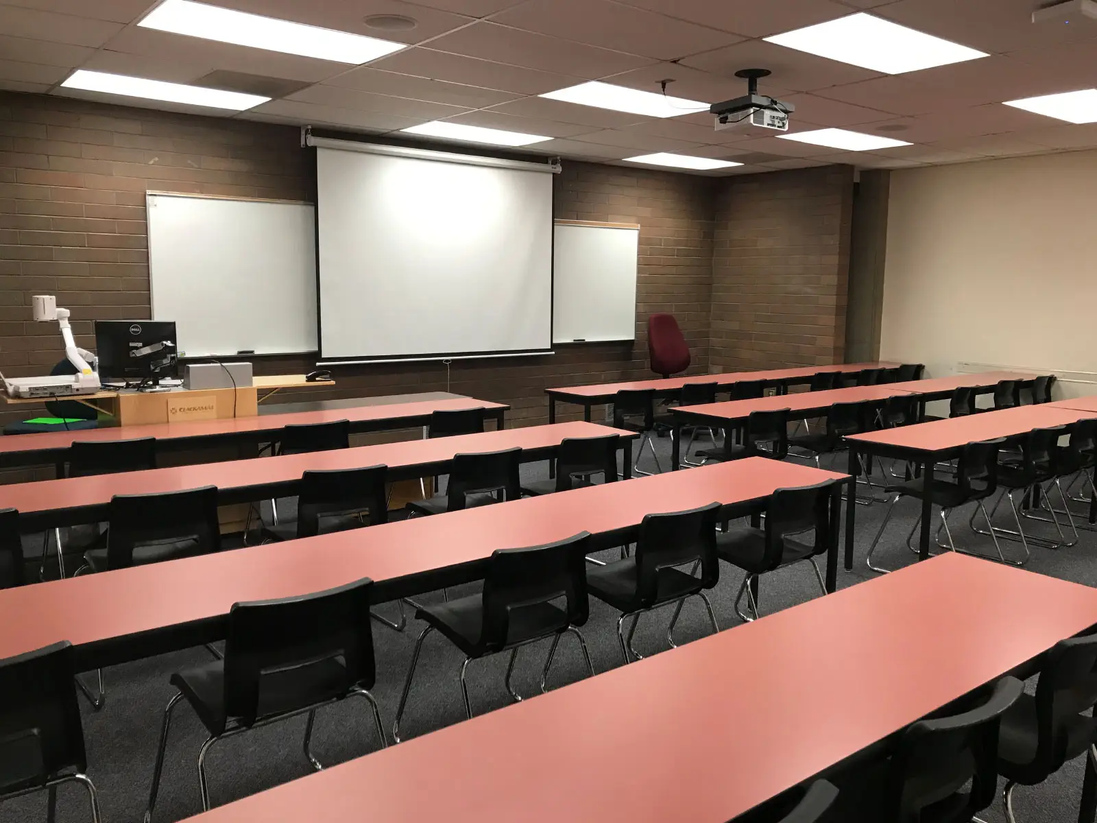 Rows of red tables and a podium in an Oregon CIty classroom with a projector screen against a brick wall Rows of red tables and a podium in an Oregon CIty classroom with a projector screen against a brick wall