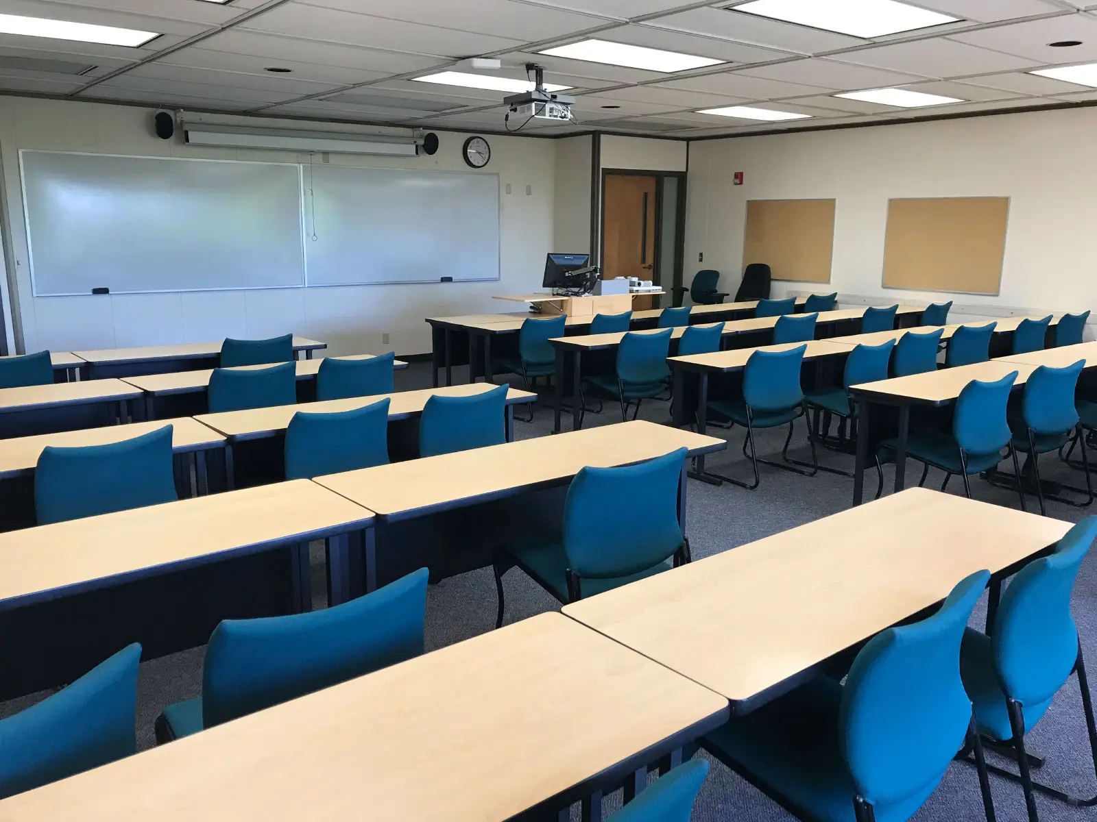 Rows of tables with blue chairs in a classroom with a large whiteboard and projector