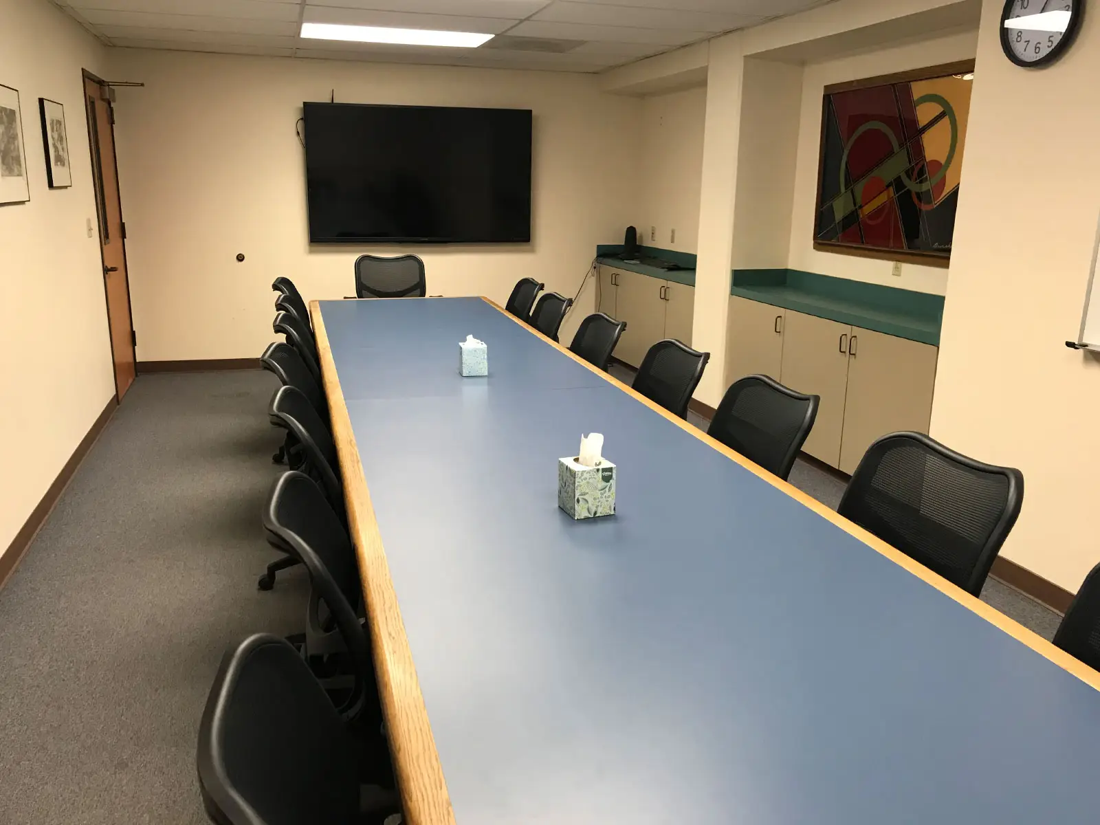 A long, blue table with several chairs in a conference room with a TV display on the Oregon City campus