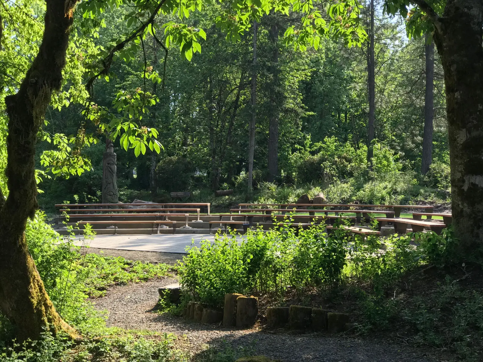 Trees, grass and a gravel path in front of the ELC amphitheater with rows of seats, at the Oregon City campus