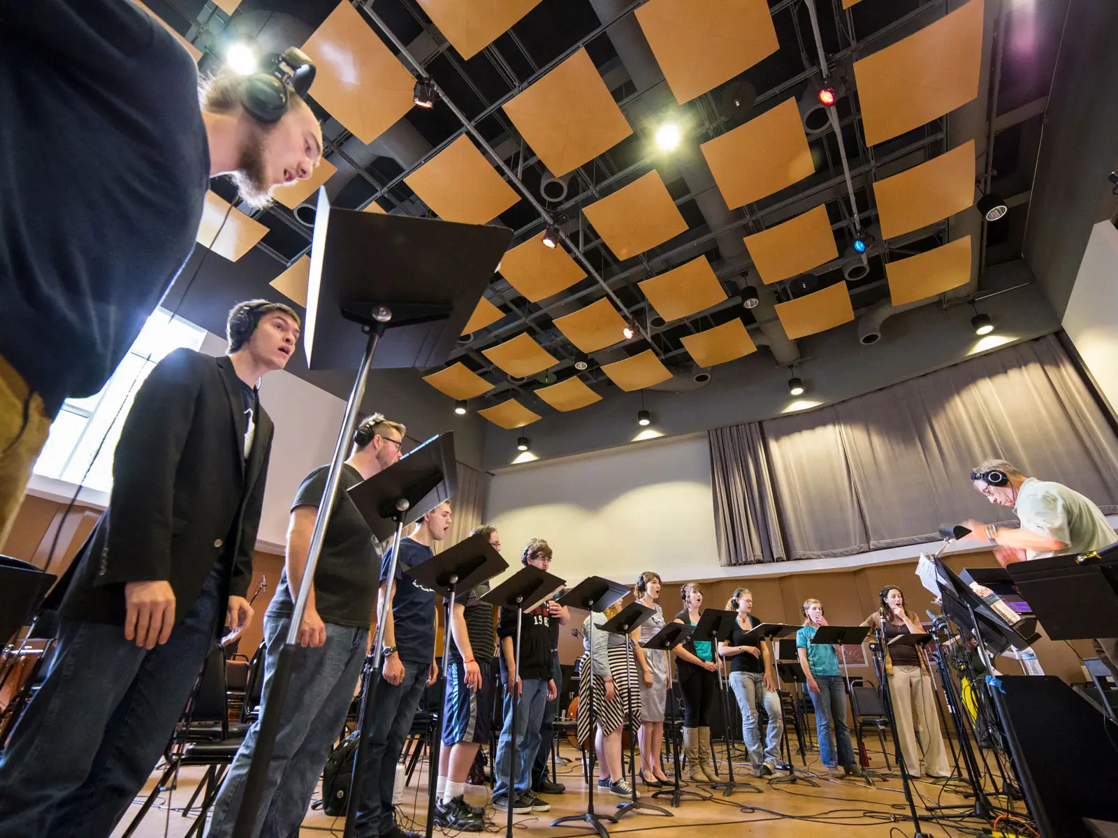 Singers in the recording hall with instructor and several music stands at the Niemery Center